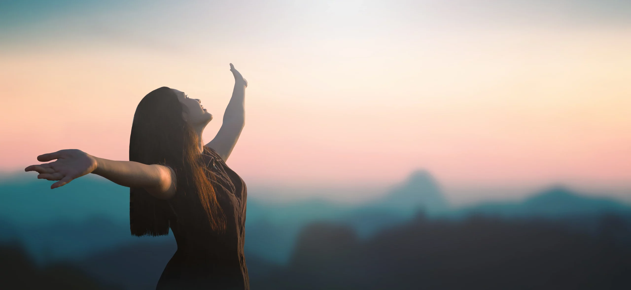 Une femme ouvre les bras face à un horizon lumineux